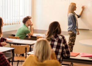 Smiling female student solving mathematic formula on whiteboard with her teacher during lecture in the classroom.